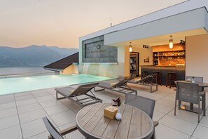 Un espace piscine extérieur moderne, doté de chaises longues, d’un bar et offrant une vue sur les montagnes.