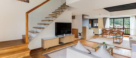 Una sala de estar moderna con una escalera de madera, un televisor de pantalla plana, un comedor con muebles de madera y un ventanal con vistas al exterior.