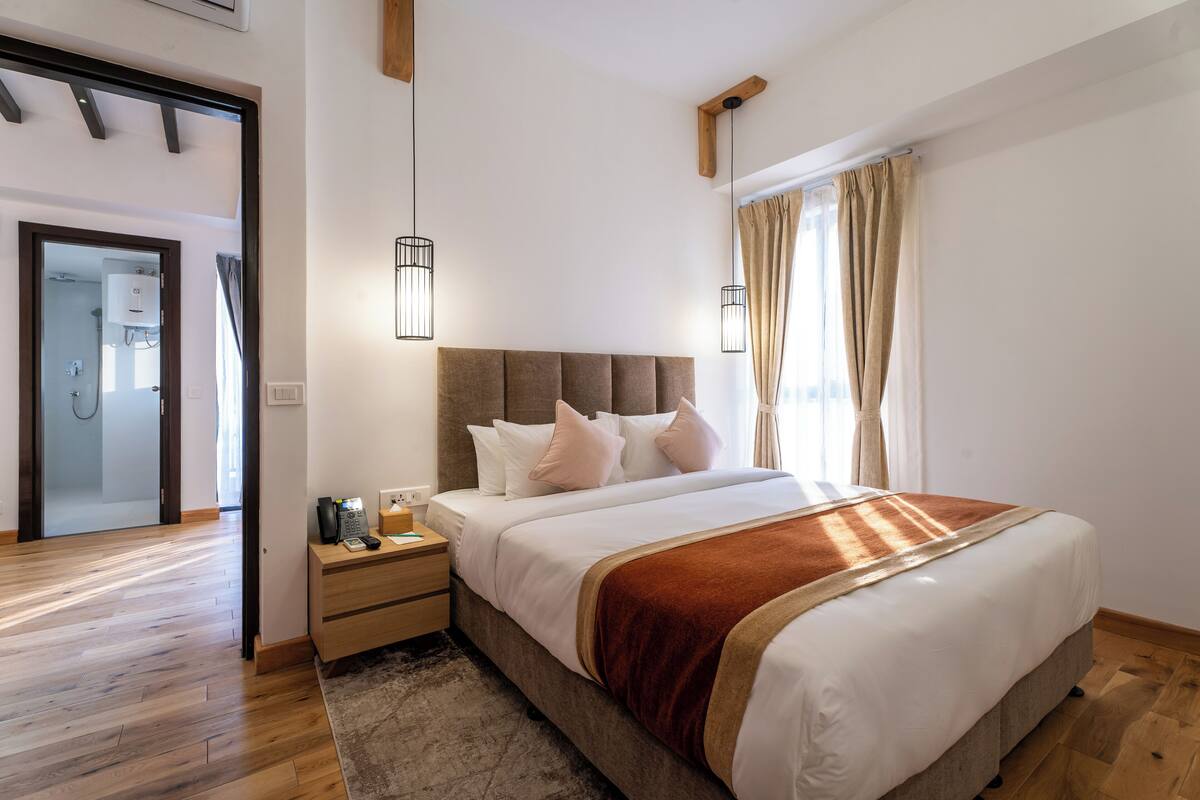 A modern bedroom with a large bed, wooden flooring, a nightstand, and a bedside table with a lamp.