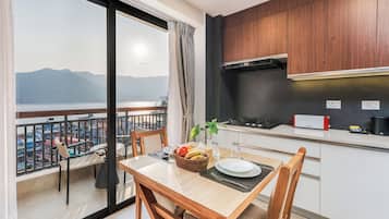 Una cocina moderna con vista a un lago y montañas, un comedor con mesa dispuesta para dos personas y un balcón con vistas.