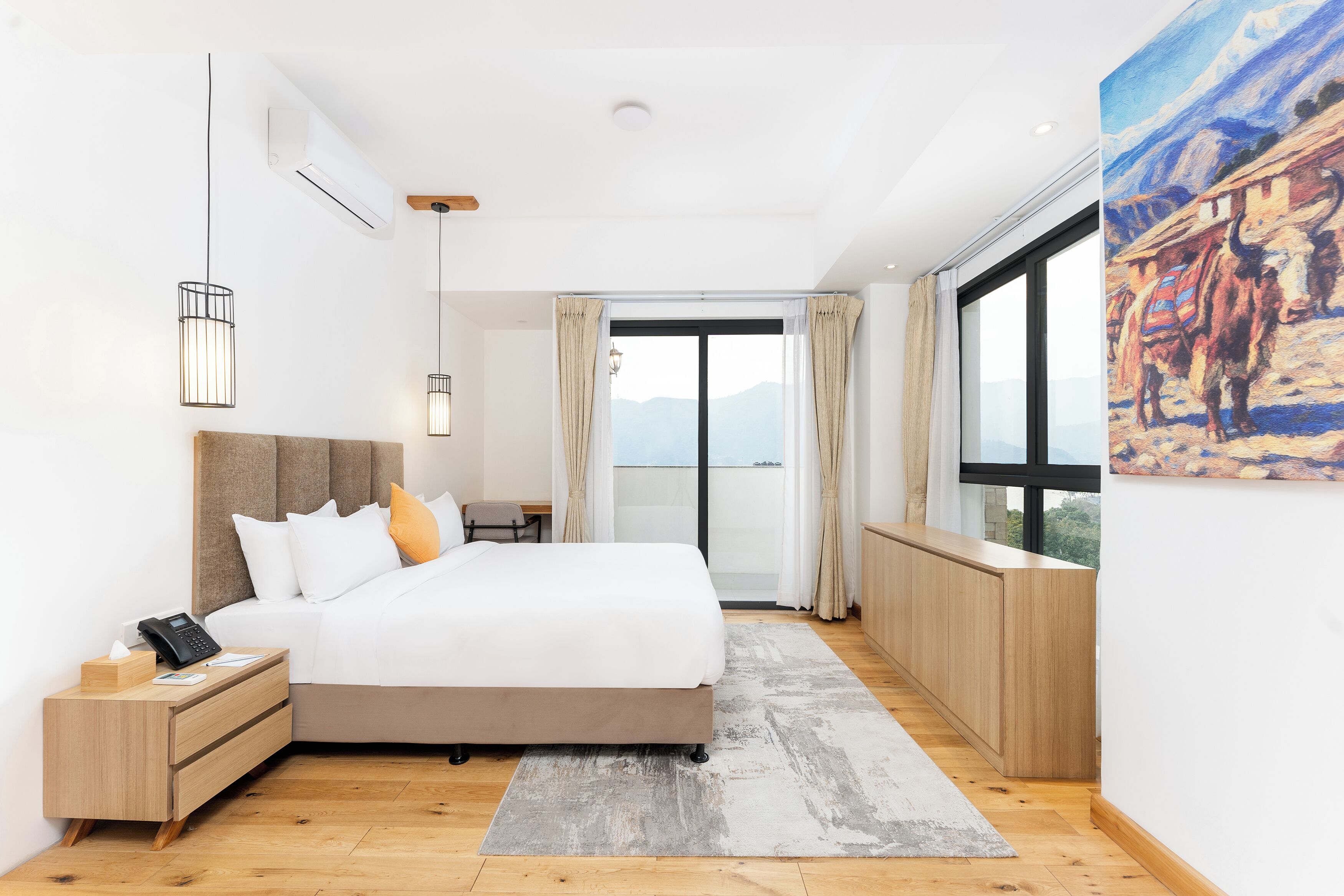 A modern hotel room with a large bed, bedside table, and a view of the mountains through the window.