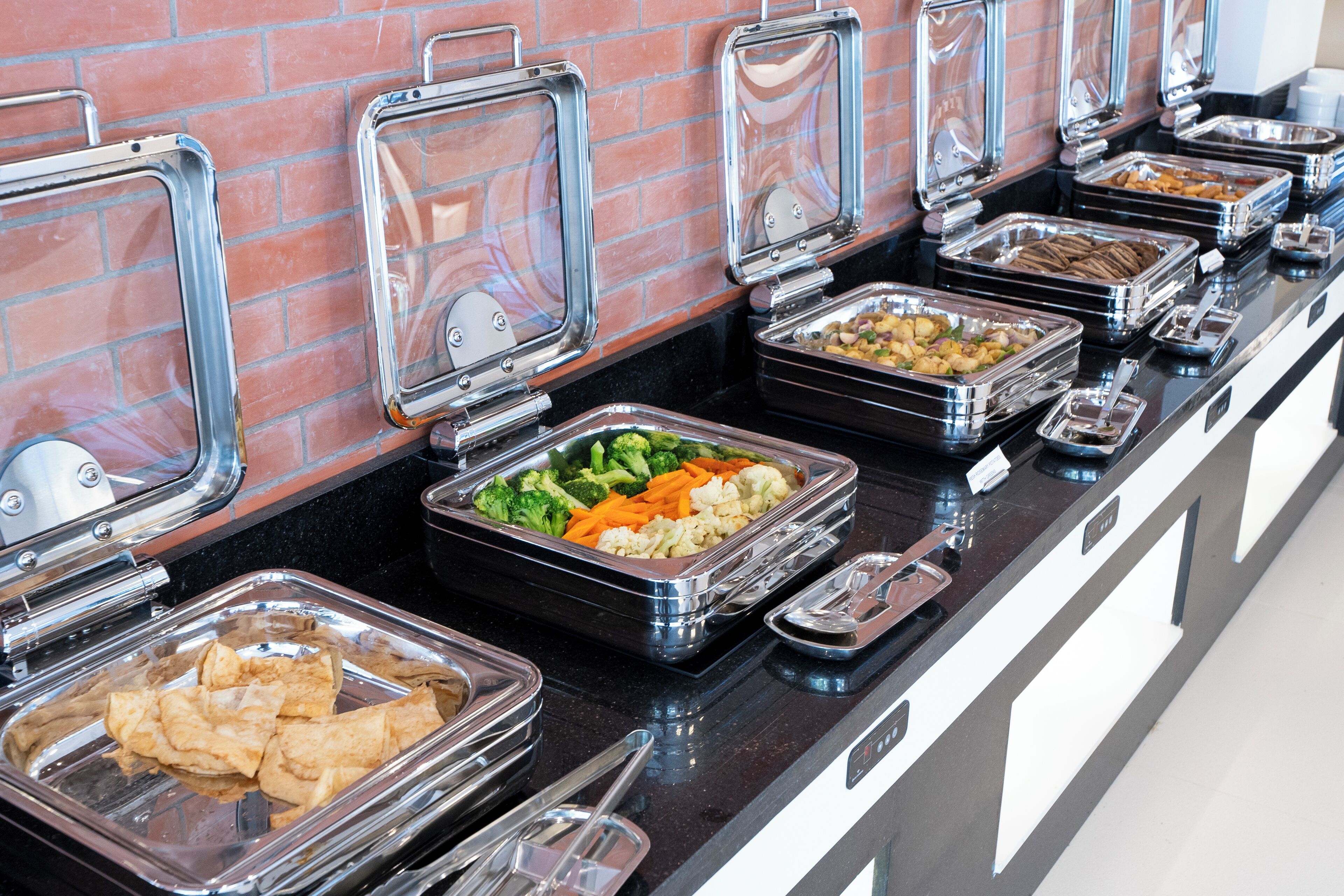 A buffet with various food items in clear containers, arranged on a black countertop with a brick wall in the background.