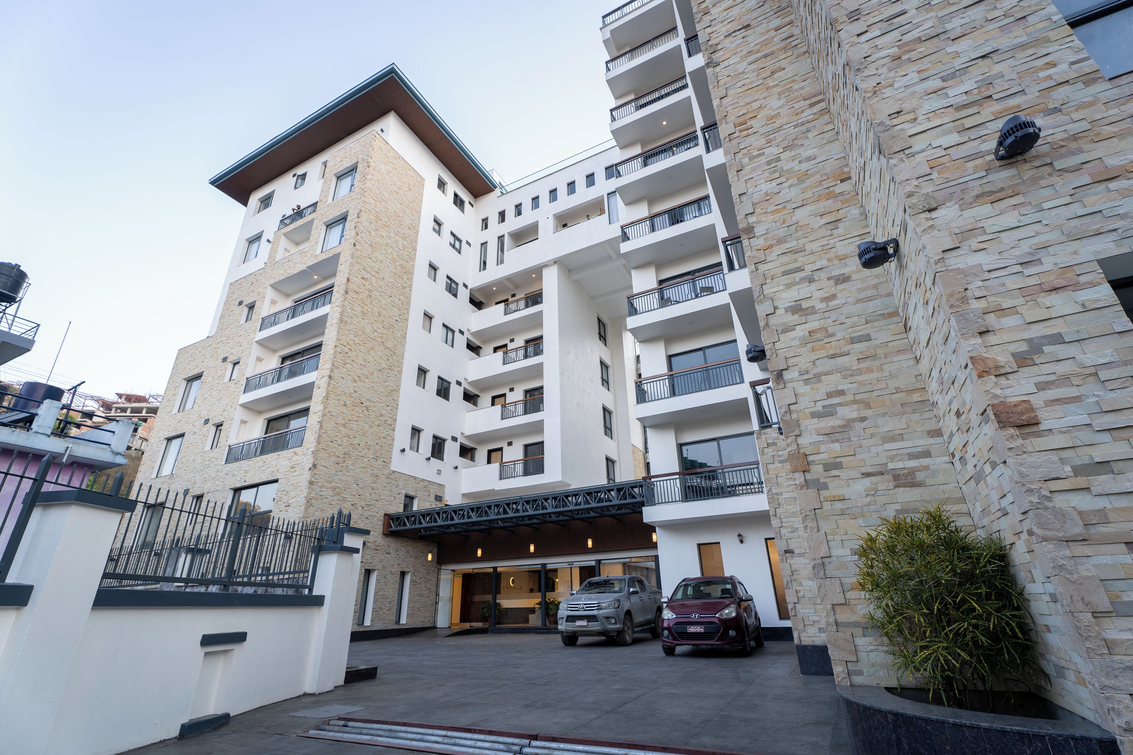 Un hotel de varios pisos con fachada de piedra, balcones y un estacionamiento con coches.
