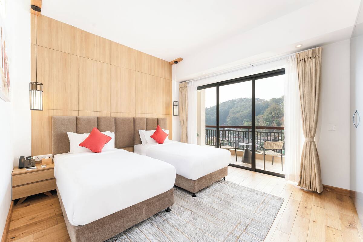 A hotel room with two beds, a wooden headboard, a large window with a view, and a balcony.