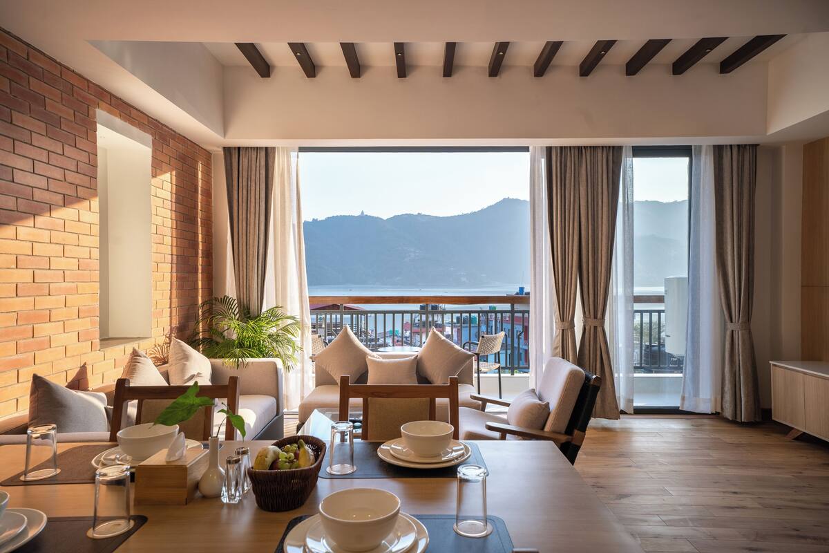 A dining area with a view of mountains, a brick wall, and a balcony with curtains.
