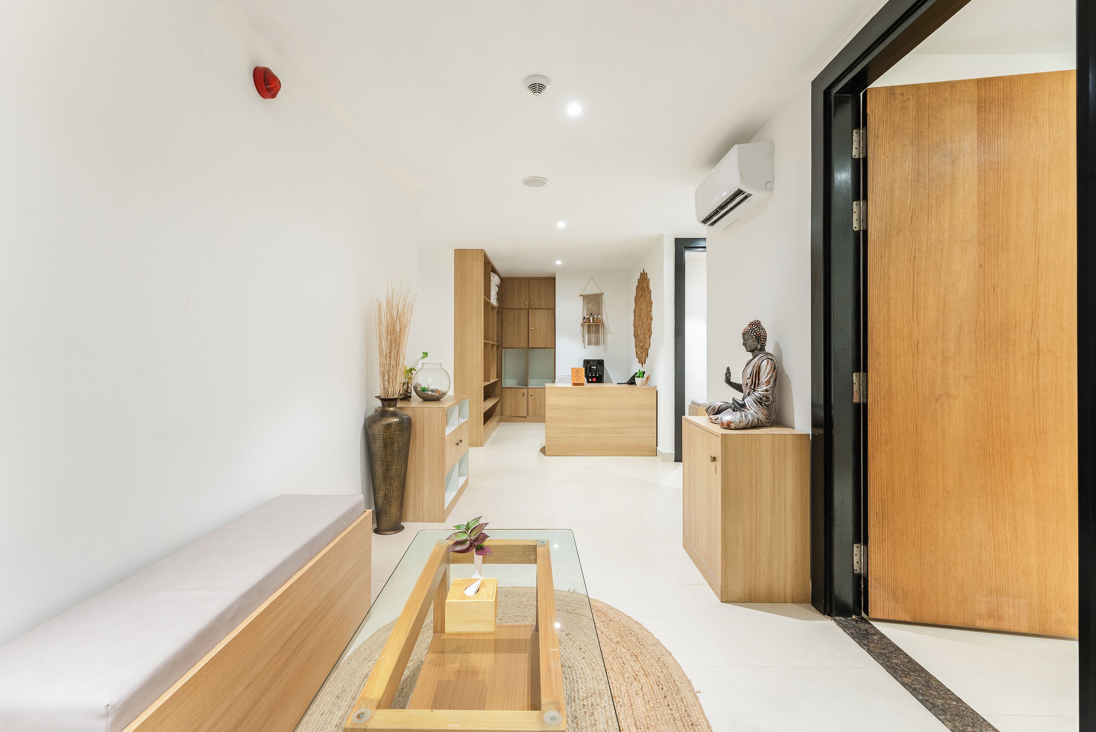 Ein modernes Interieur mit einer Rezeption, Holzschränken, einer Statue und einem Glastisch mit Pflanze.