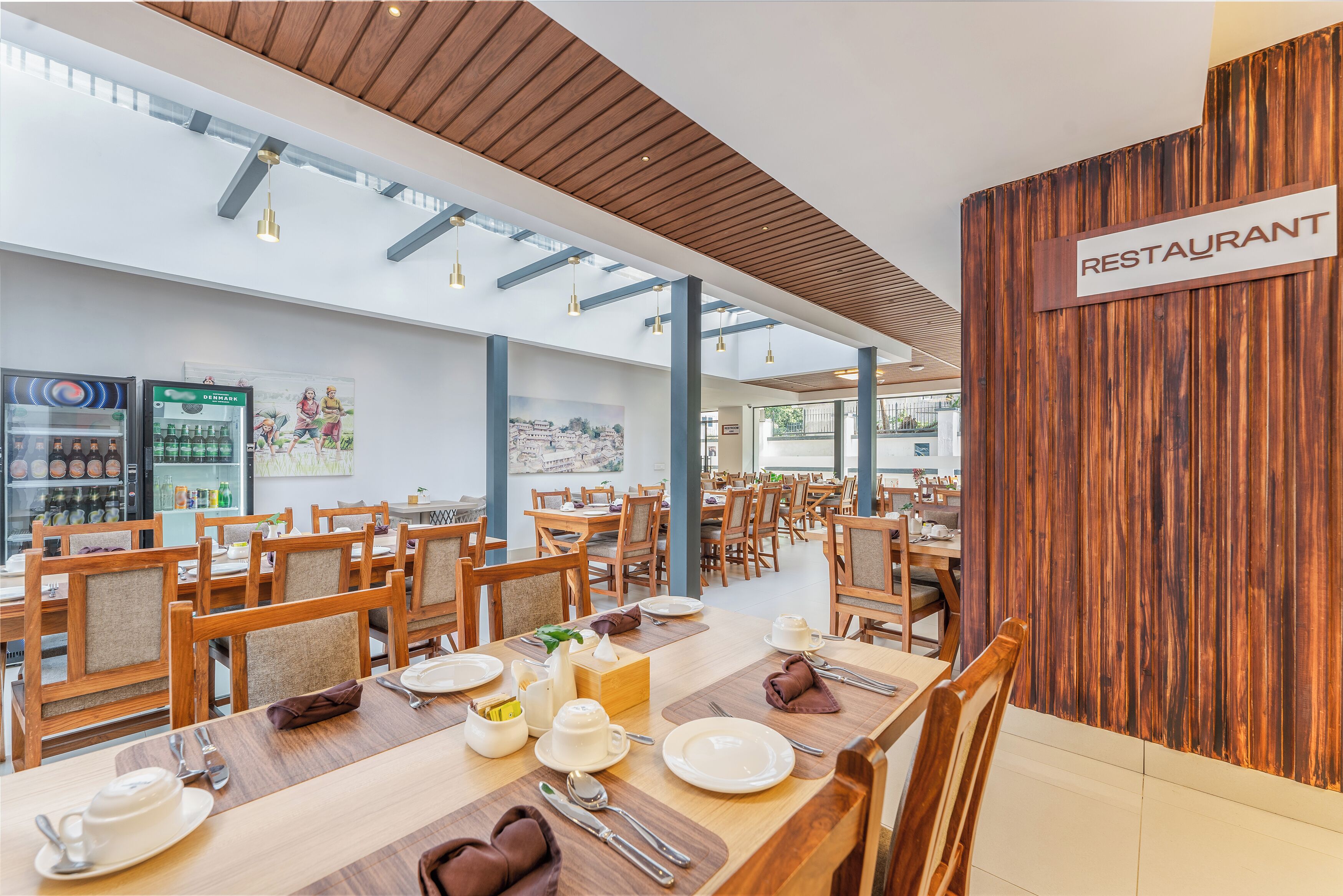 Een restaurant met houten tafels en stoelen, een bord dat het restaurantgedeelte aangeeft en een uitzicht op de eetruimte.
