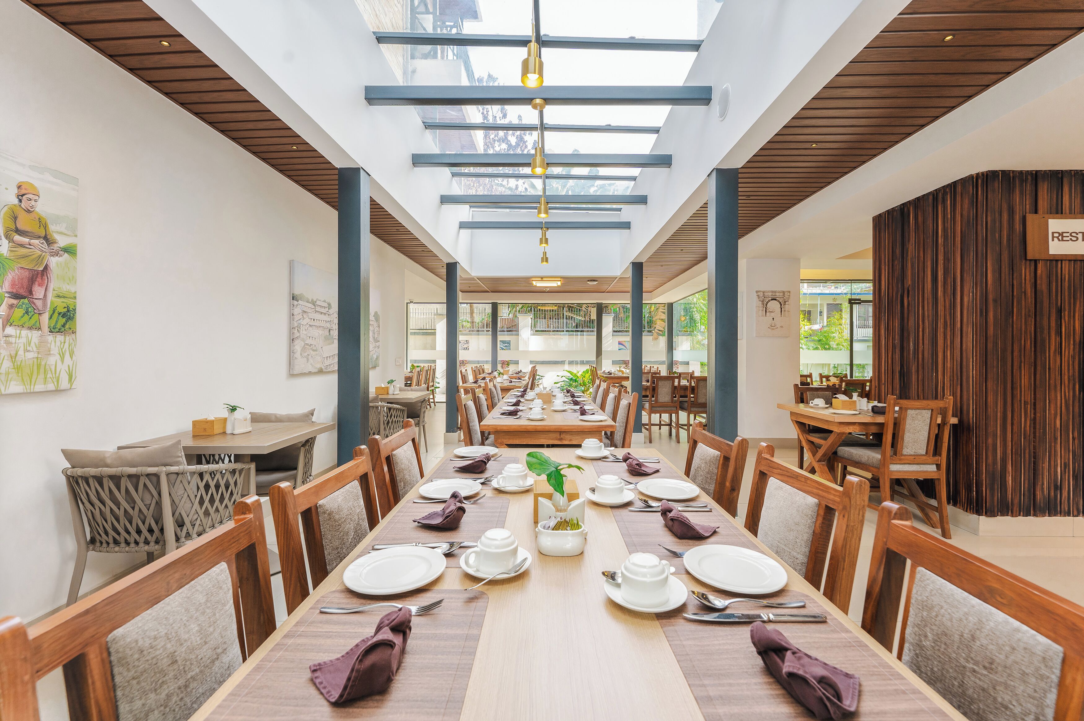 A restaurant with a long dining table set for a meal, wooden chairs, and a high ceiling with skylights.