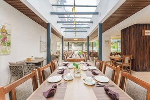 Un ristorante con un lungo tavolo imbandito per un pasto, sedie in legno e un soffitto alto con lucernari.