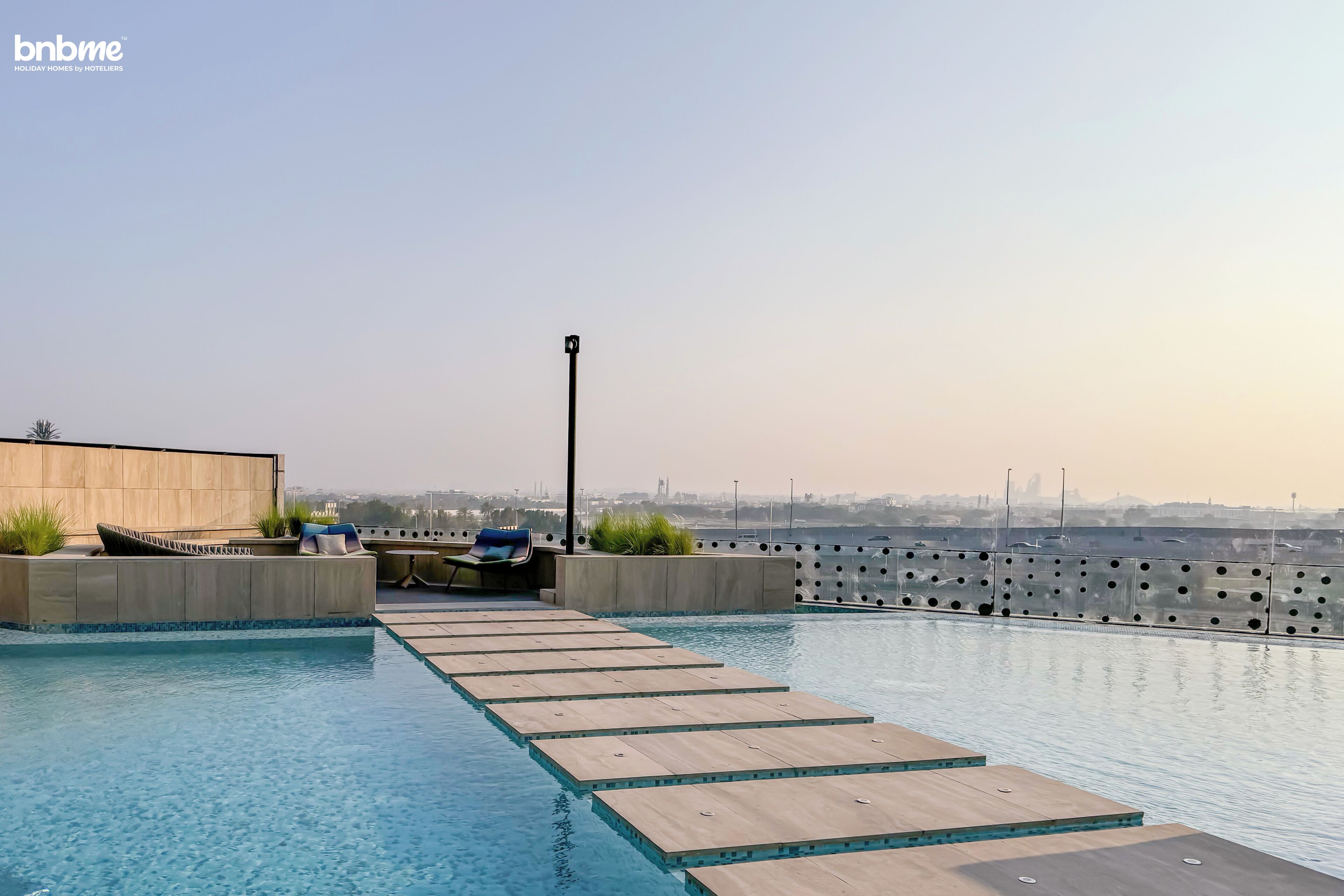A rooftop pool with a clear view of the city skyline, a seating area with a chair and a table, and a modern architectural design.