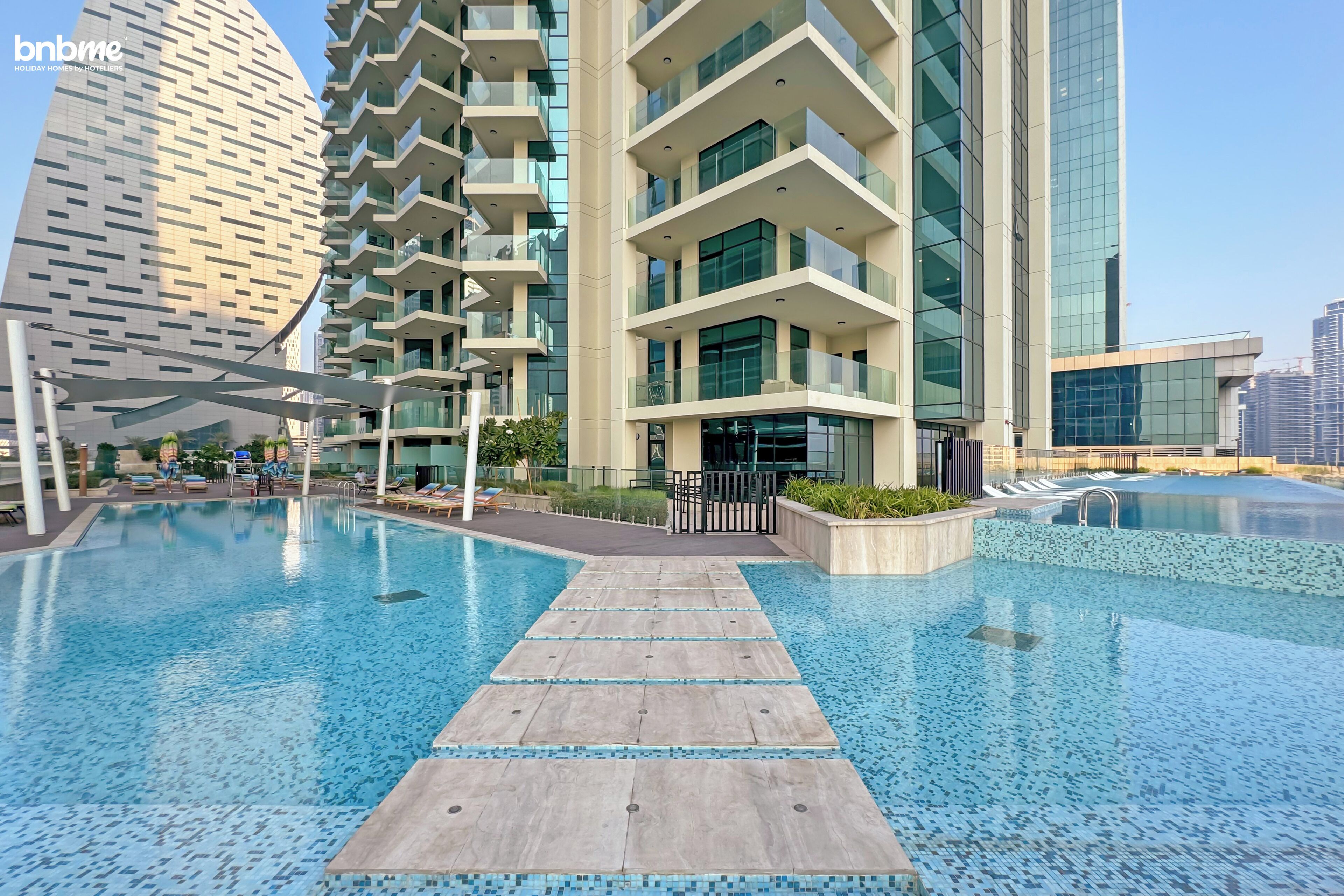 A modern hotel with a swimming pool, multiple balconies, and contemporary architecture.