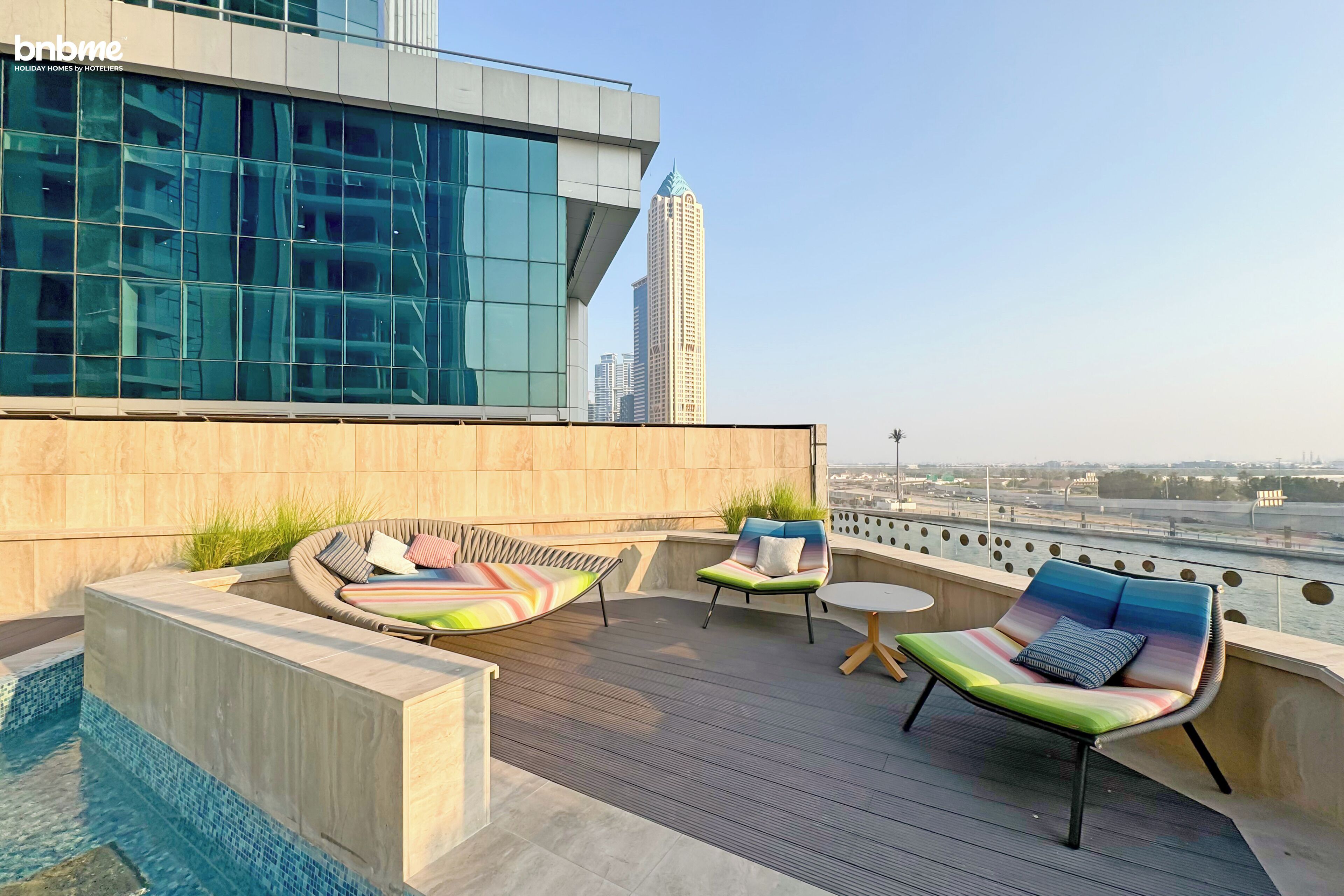 A rooftop terrace with a pool, lounge chairs, and a view of a city skyline.