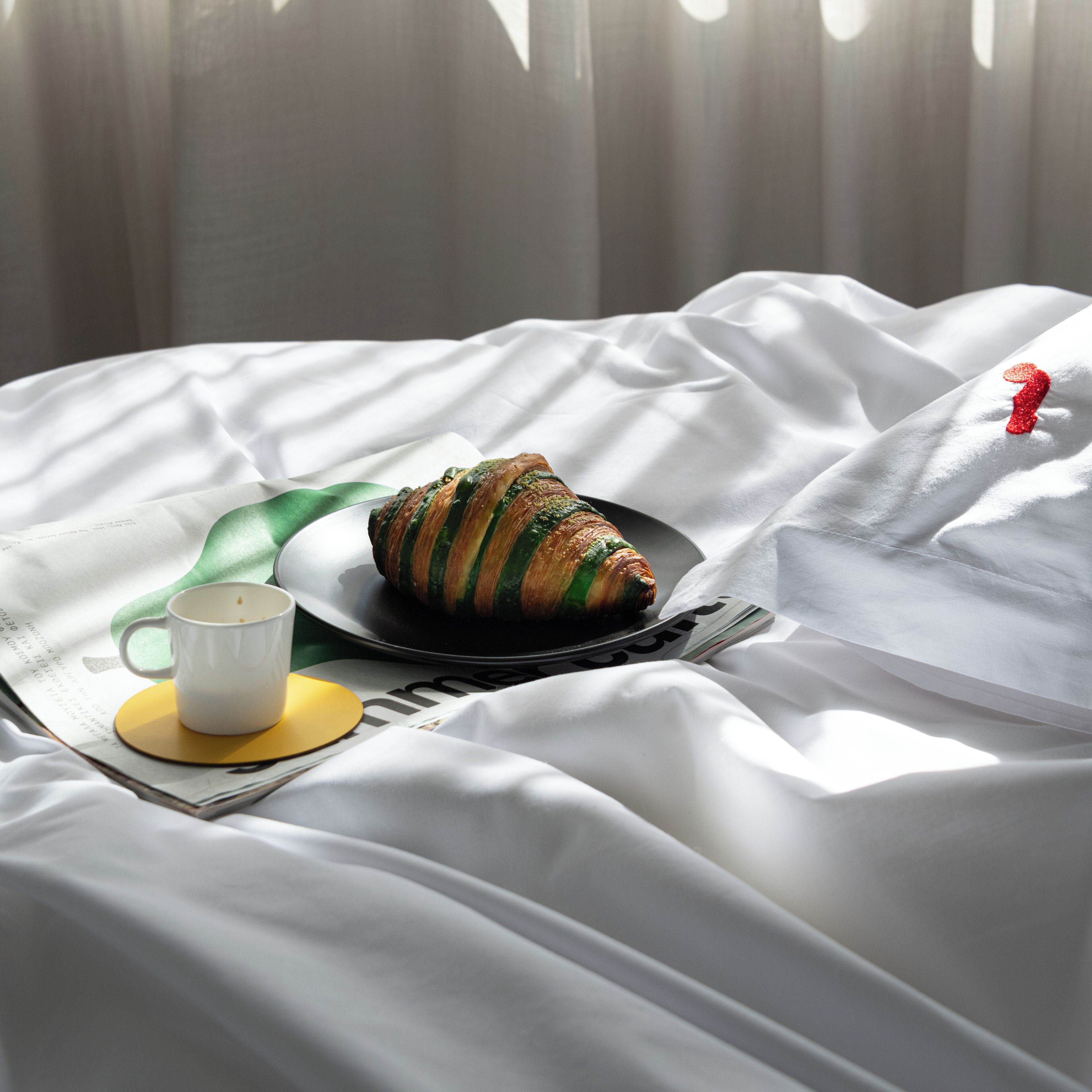 A neatly made bed with a plate of food, a cup, and a spoon.