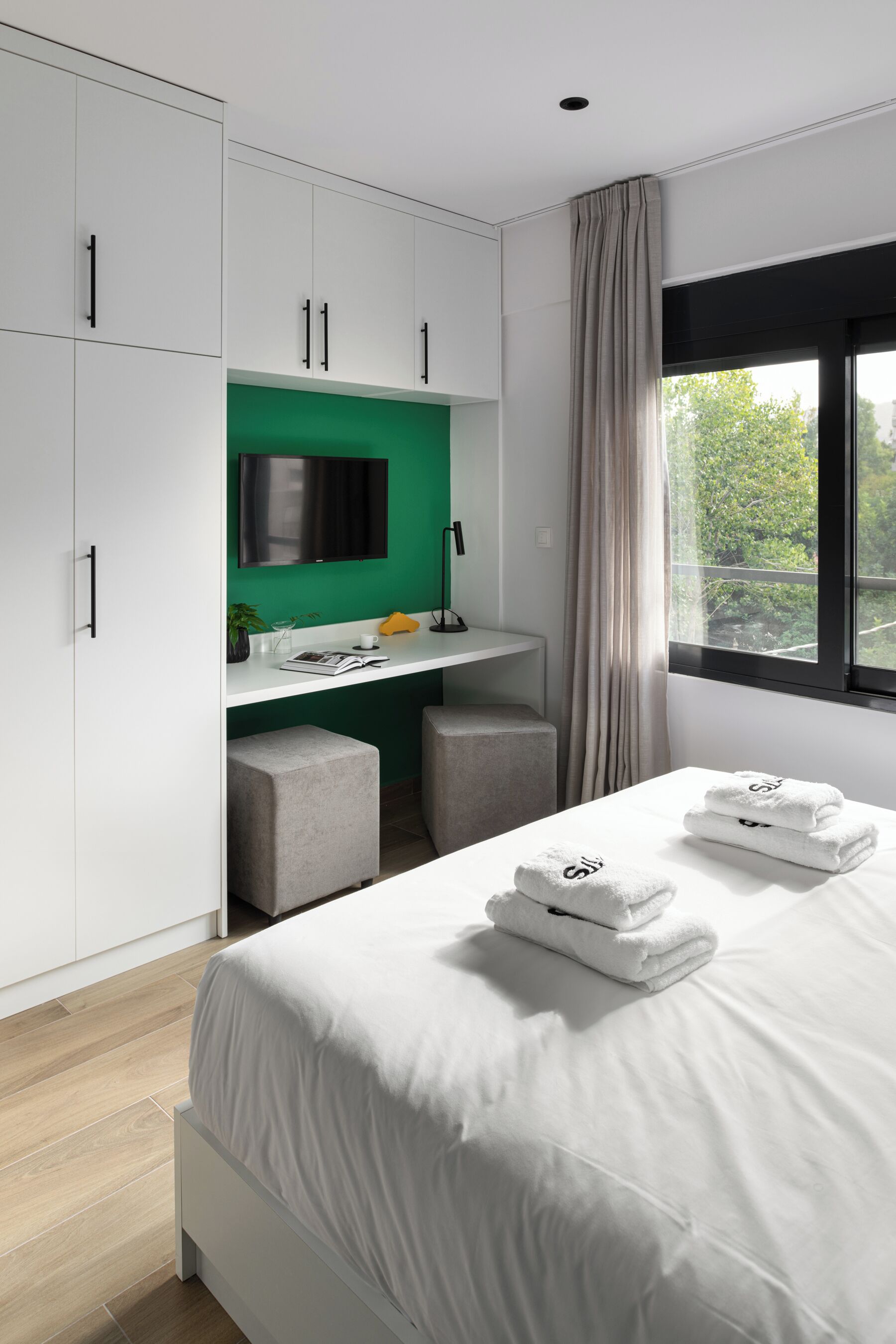 A modern bedroom with a bed, a desk, and a TV.