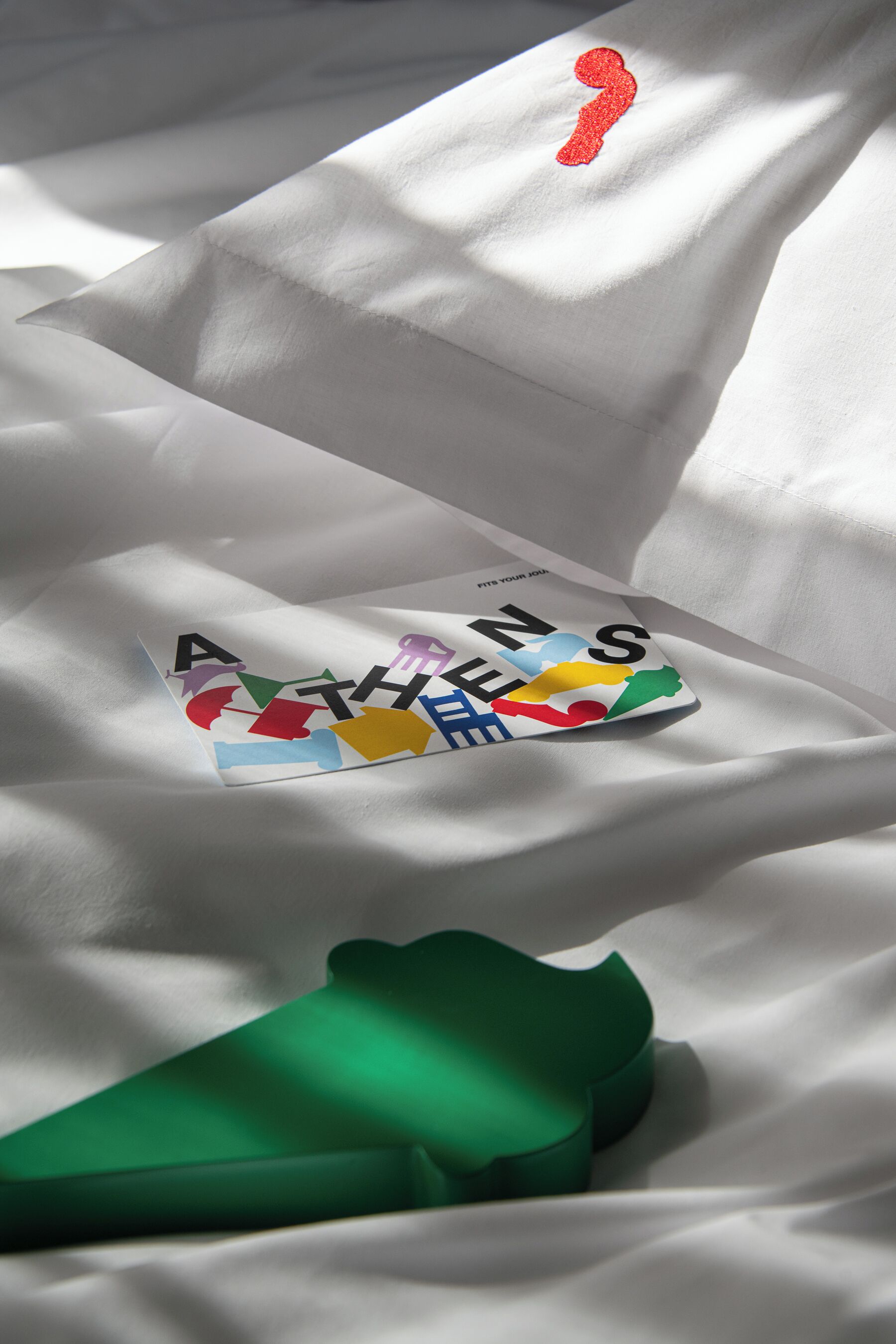 A book titled "ATHENS" on a white fabric surface with a green object partially visible.