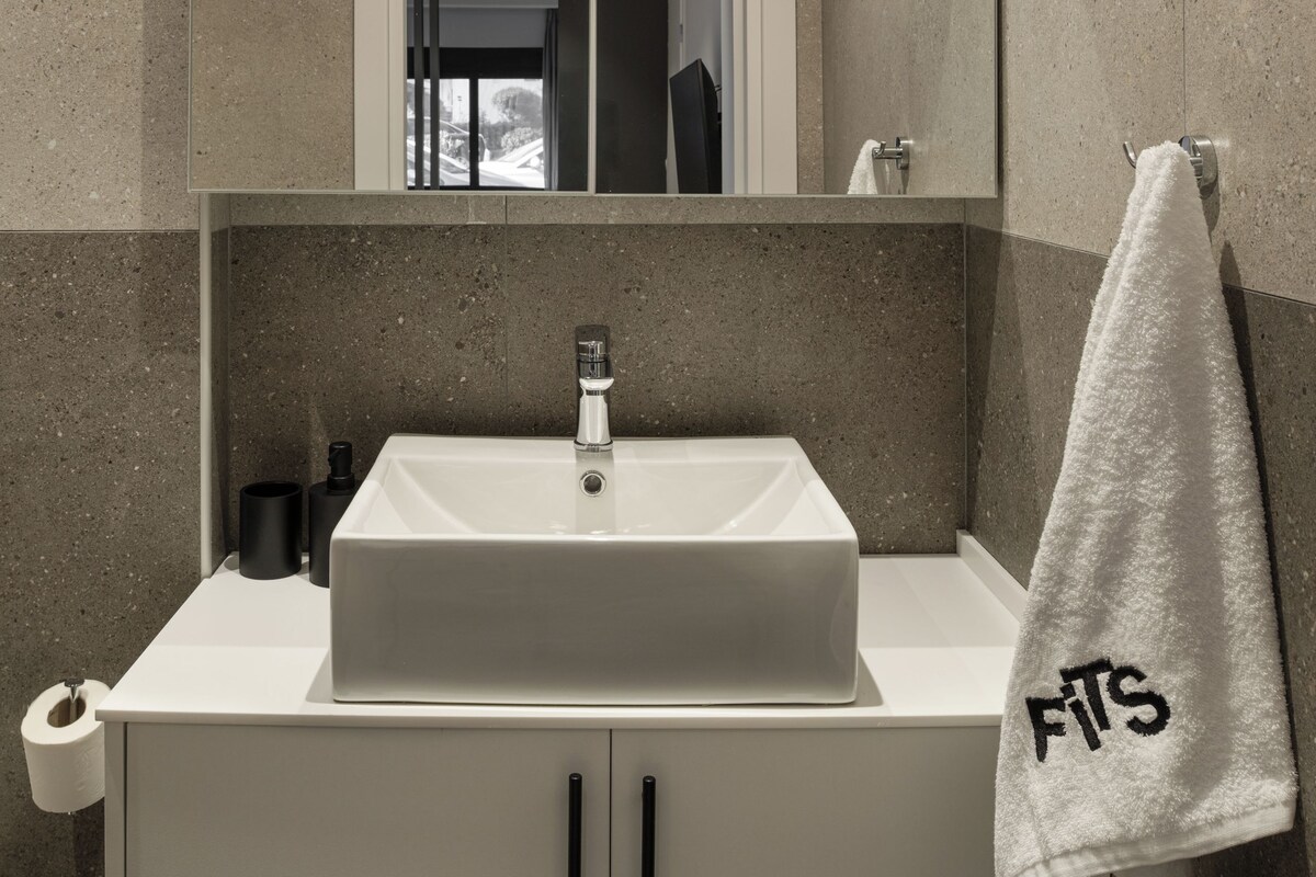 A modern bathroom with a white sink, a mirror above it, and a towel hanging on the wall.