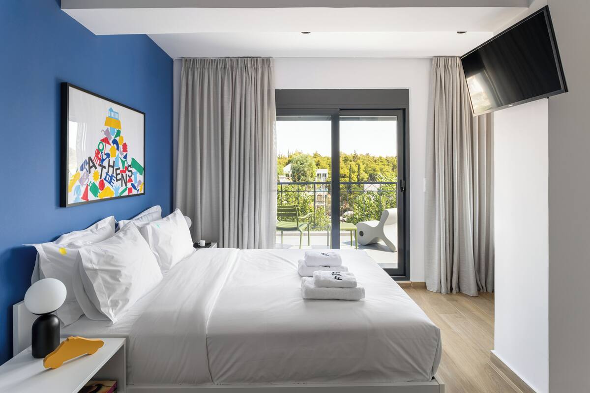 Ein modernes Hotelzimmer mit einem großen Bett, einem Flachbildfernseher, einem Gemälde an der Wand und einem Balkon mit Blick auf Grünflächen.