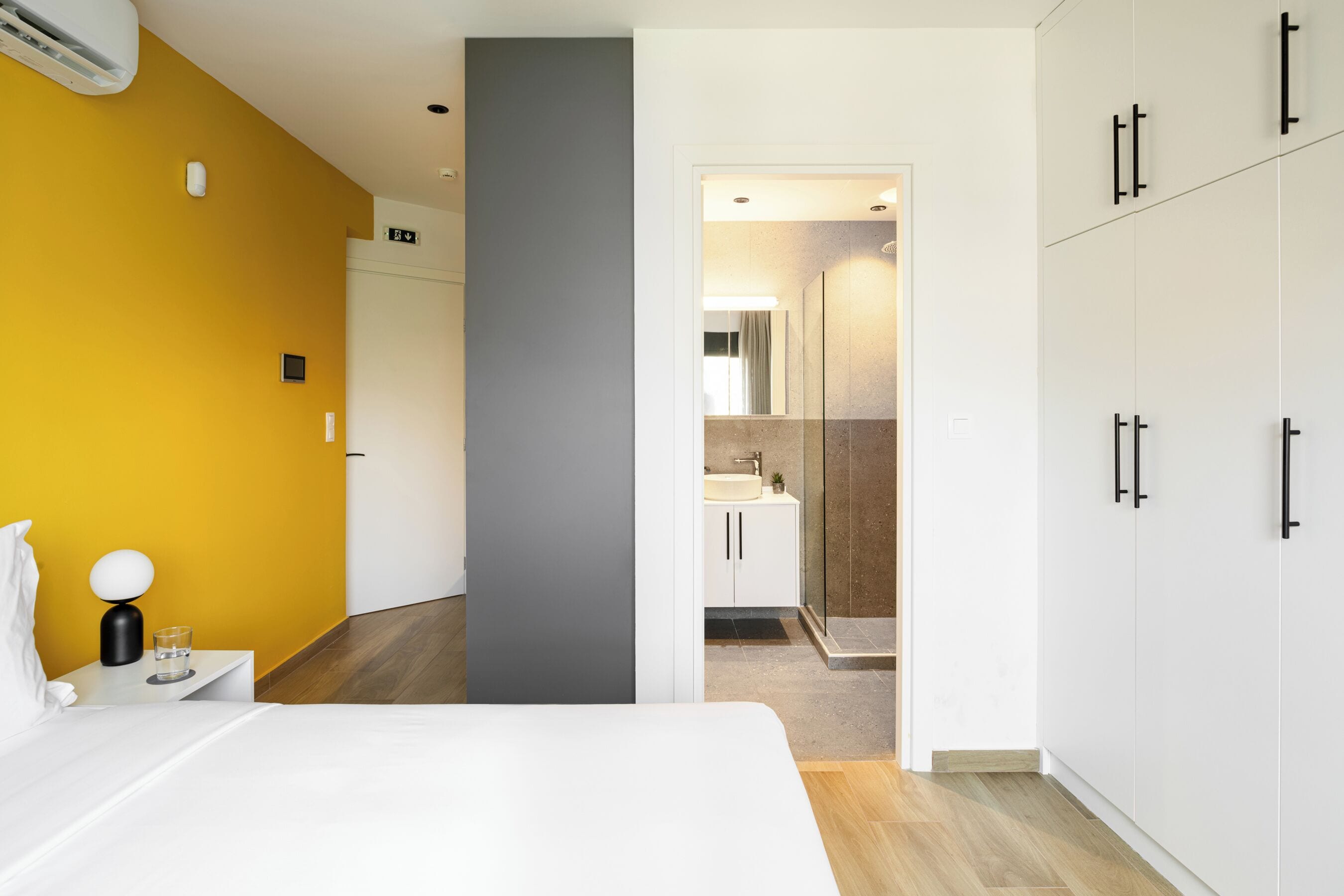 Une chambre d’hôtel avec un lit, une table de chevet avec une lampe, un verre d’eau et une vue sur la salle de bain.