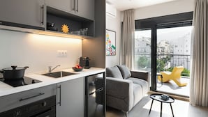 Una cucina moderna con forno integrato, lavello e piano cottura. C'è un divano grigio e un tavolino con una tazza sopra. La stanza ha un'ampia finestra con vista sugli edifici.