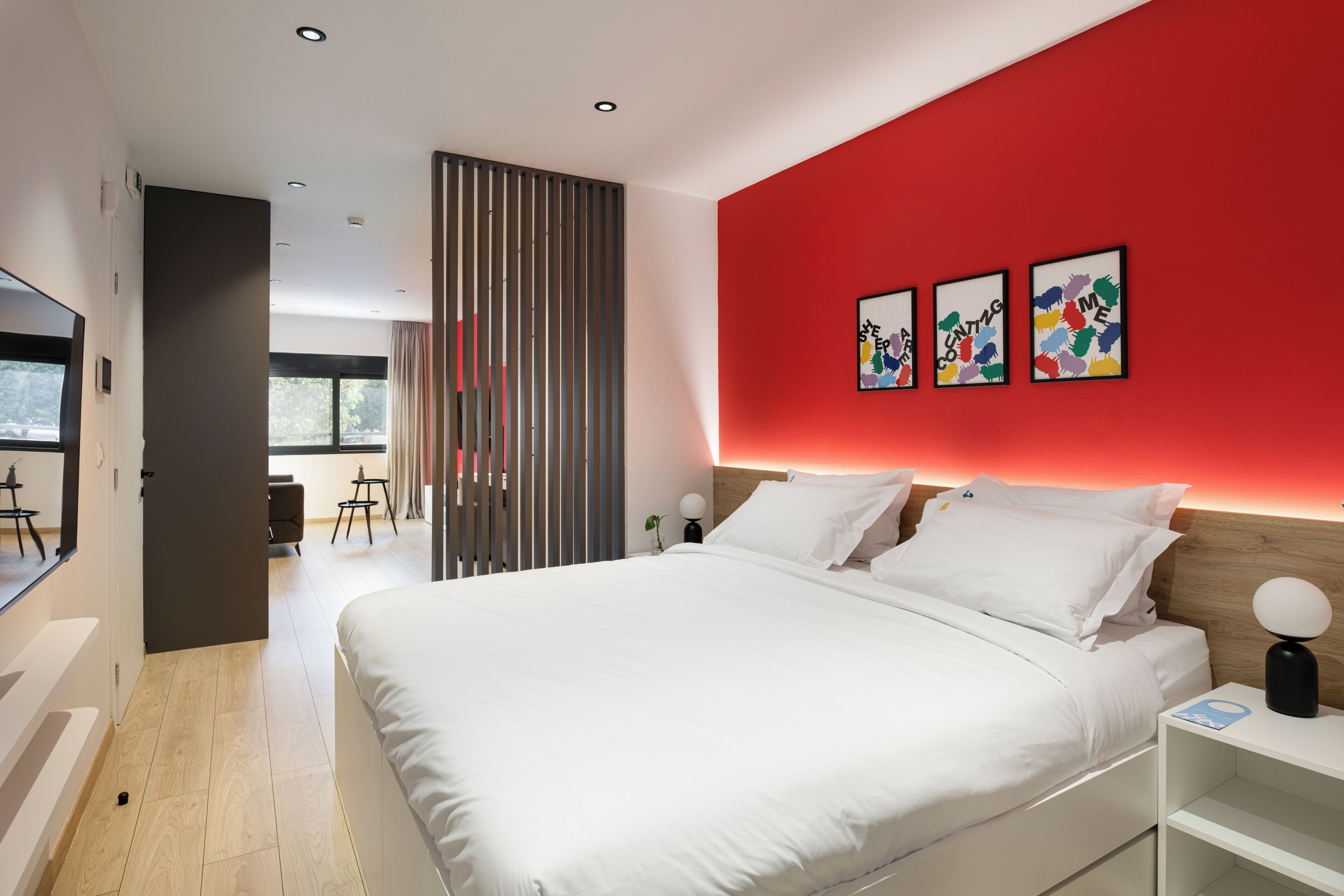 A modern hotel room with a large bed, a red accent wall, and three framed artworks.