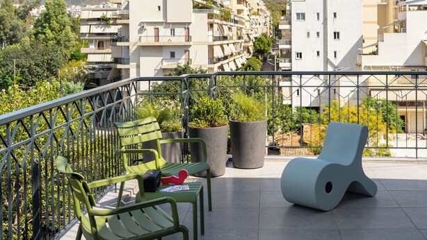 Un balcone con sedie verdi, una poltrona blu e piante in vaso.