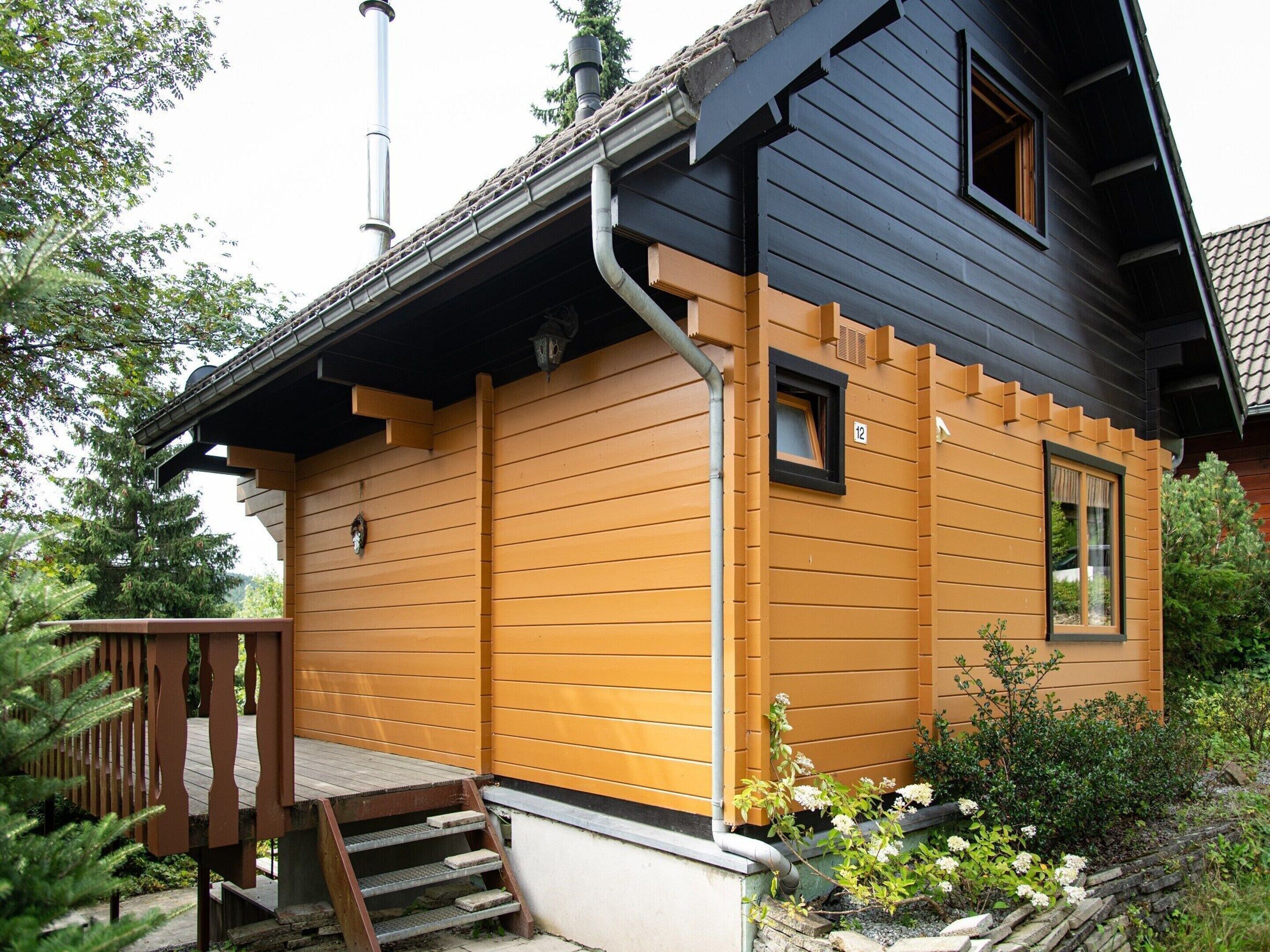 A two-story house with a wooden exterior, a small porch with steps, and a chimney.