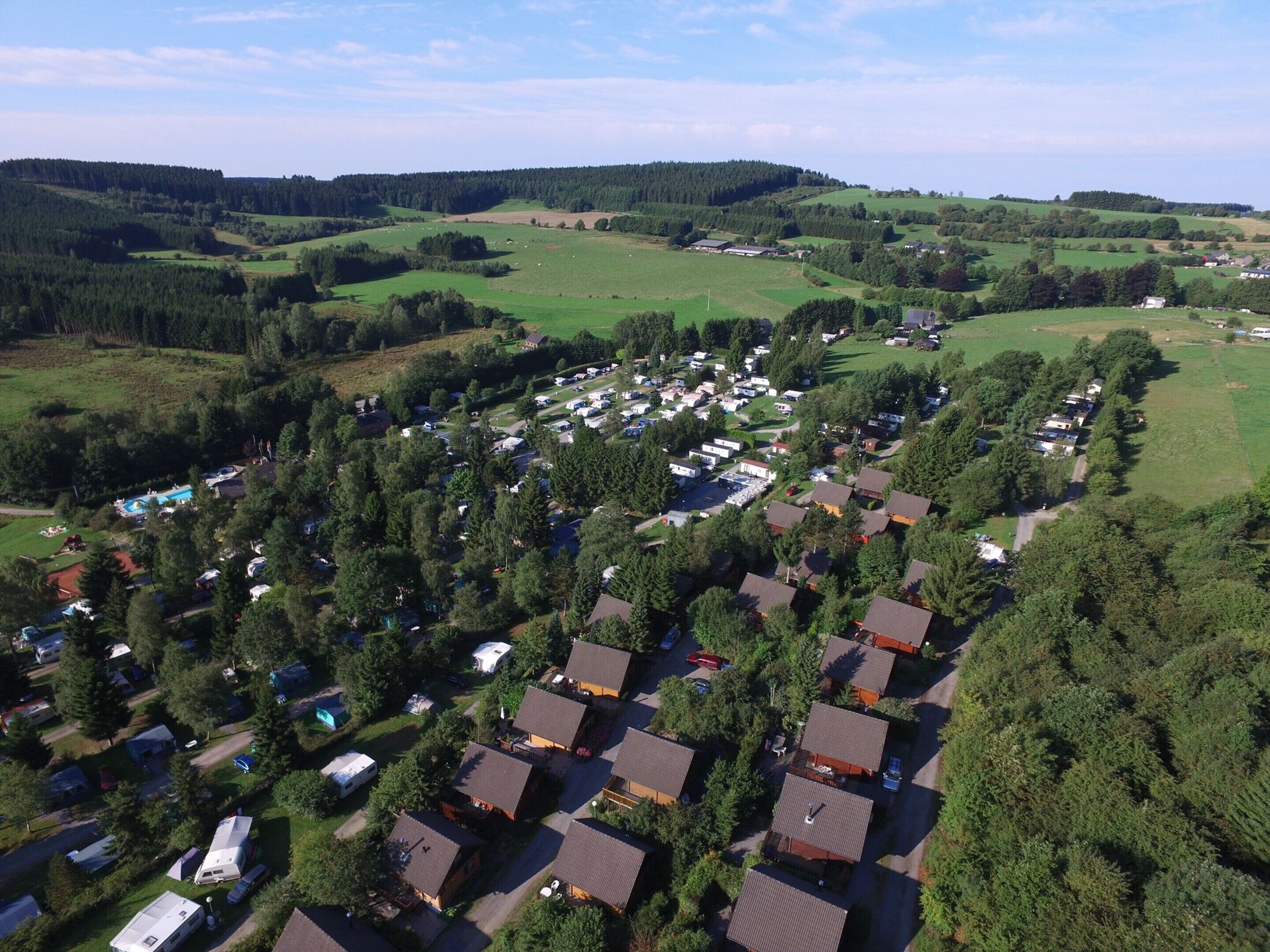 Luchtbeeld van een woongebied met huizen en stacaravans, omgeven door groen en heuvels.