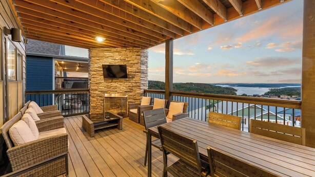 A covered deck with outdoor furniture, a stone wall, and a TV screen. - House of FUN! Games, Lakeview, Bunkroom! (Branson)