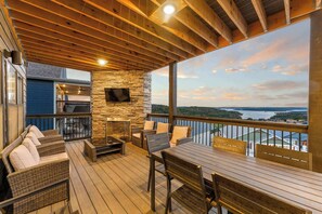 Une terrasse couverte, aménagée avec du mobilier d’extérieur, un mur en pierre et un écran de télévision.