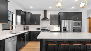 A modern kitchen with dark cabinets, a large island, stainless steel appliances, and bar stools. - House of FUN! Games, Lakeview, Bunkroom! (Branson)