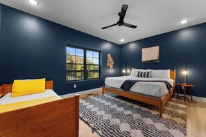 Une chambre à coucher avec un lit, une table de chevet avec une lampe, une fenêtre et un ventilateur de plafond.