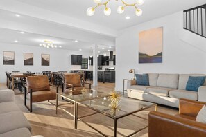 A modern living room with a sofa, armchairs, a glass coffee table, and a dining area with chairs and a table. - House of FUN! Games, Lakeview, Bunkroom! (Branson)