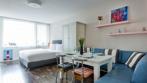 Moderni hotellihuone, jossa on sänky, ruokapöytä, sohva ja pieni keittiö.