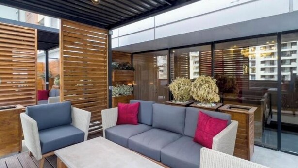 An outdoor seating area with a modern design, featuring a grey sofa and chairs, wooden slats, and a glass wall reflecting the surrounding buildings. - Sam hotel Tbilisi (Tbilisi)