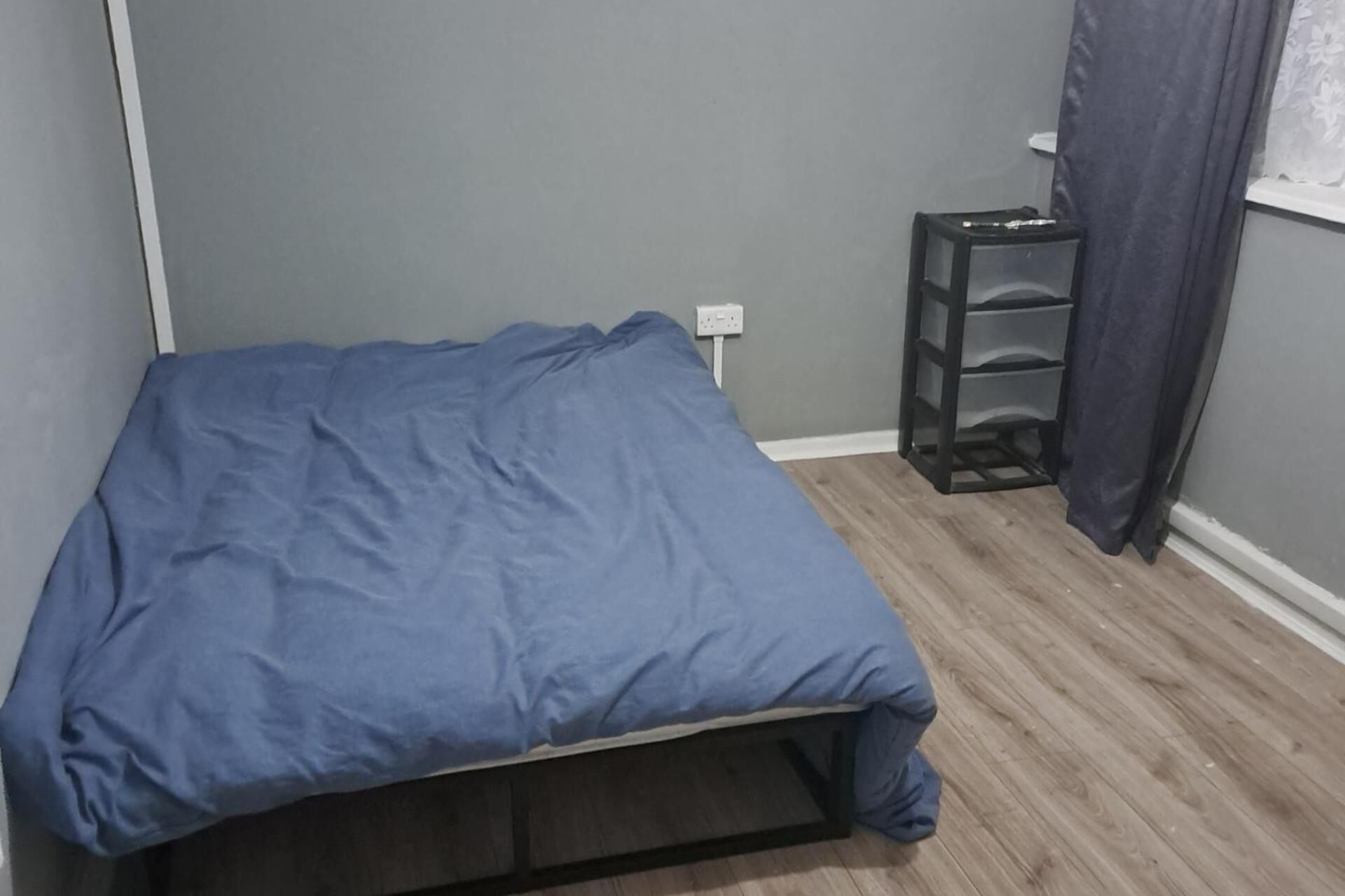 Une petite pièce avec un lit, une table de chevet et une fenêtre avec des rideaux.