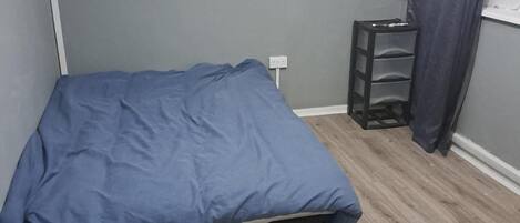 Une petite pièce avec un lit, une table de chevet et une fenêtre avec des rideaux.