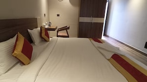 Quarto de hotel com uma cama grande, uma escrivaninha com cadeira, um guarda-roupa e uma TV na parede.