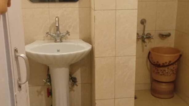 A bathroom with a pedestal sink, a mirror, a shower, and a toilet. - Narayana Greens By GRB (Sherghati)