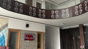 Um hall amplo com piso de mármore, corrimão curvo com painéis decorativos e uma tela de televisão na parede.