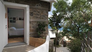 A bedroom with a stone wall, a wooden bench, and a view of the sea. - Blu70 (Staletti)