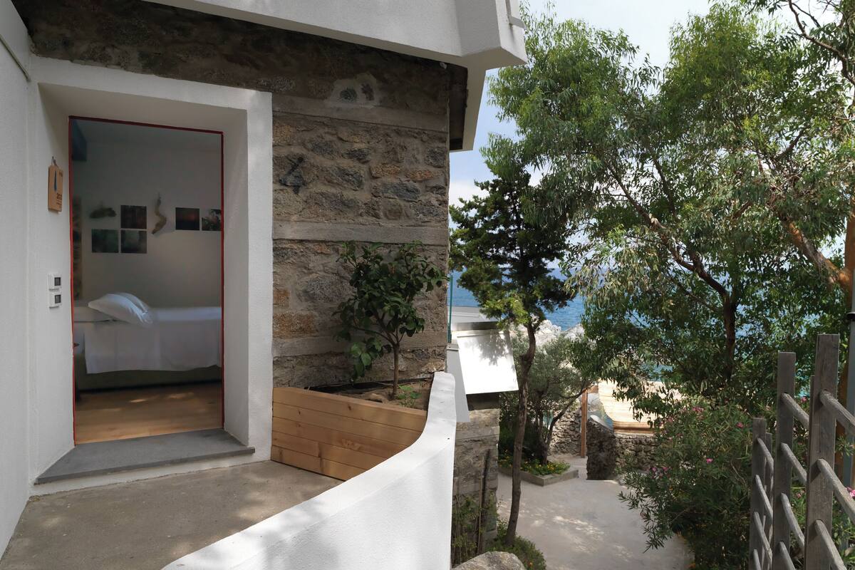 A bedroom with a stone wall, a wooden bench, and a view of the sea.