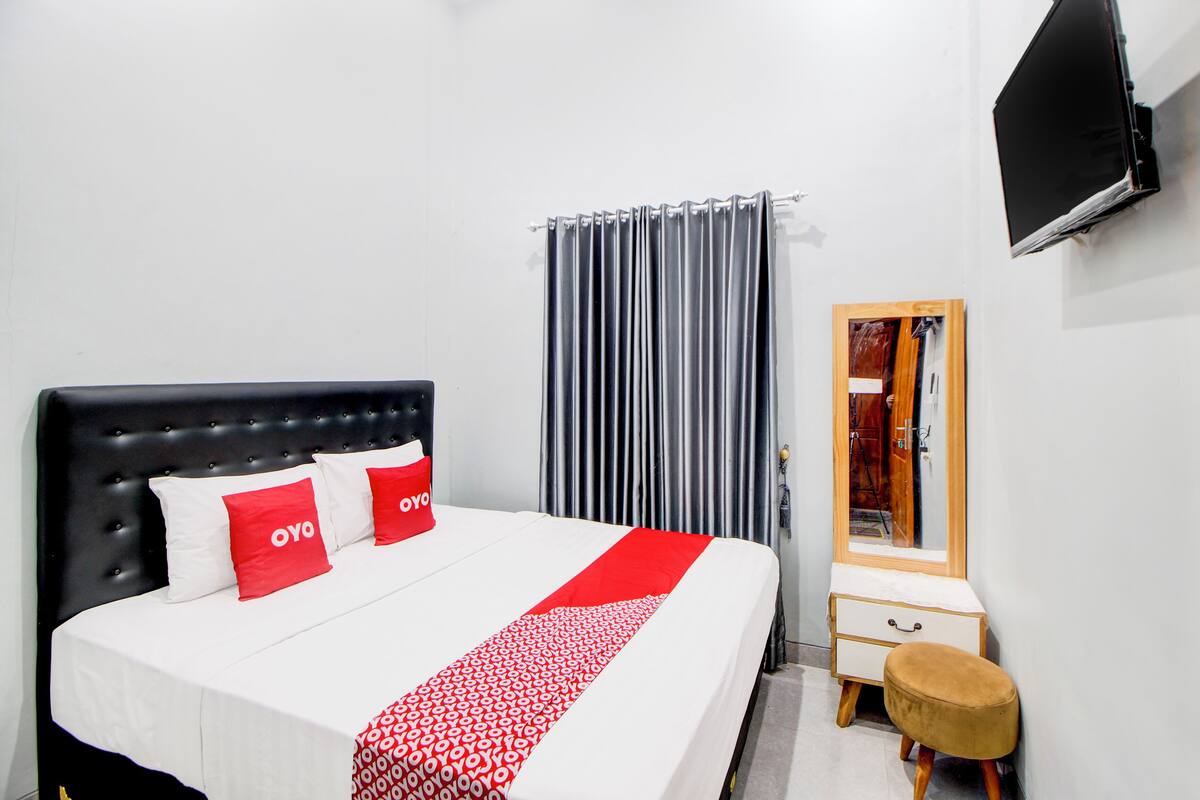A hotel room with a bed, a small bedside table, a mirror, and a TV mounted on the wall.