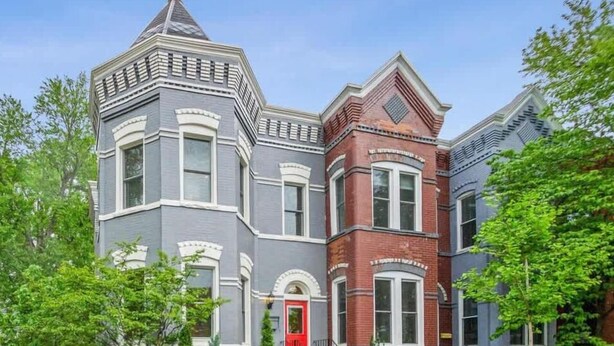 A Victorian-style house with a red door, a brick section, and a grey facade.