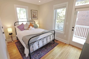 A bedroom with a bed, a window, a door, and a nightstand with a lamp.