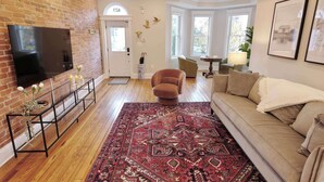 A living room with a brick wall, a flat-screen TV, a sofa, a patterned rug, and a door with a small window.