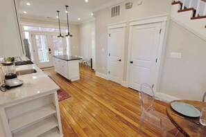 A modern kitchen with a central island, wooden flooring, and a dining area with a table and chairs.