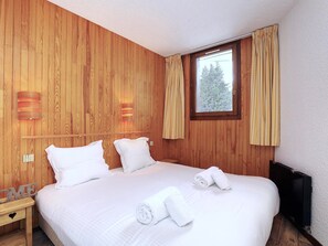 Ett hotellrum med en väggpanel av trä, en stor säng med vita sängkläder, två sänglampor och ett fönster med gardiner.