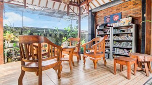 A wooden deck with chairs and a table, a bookshelf with books, and a brick wall with a Target sign. - Hotel O Maryam Homestay Syariah 2 (Patuk)