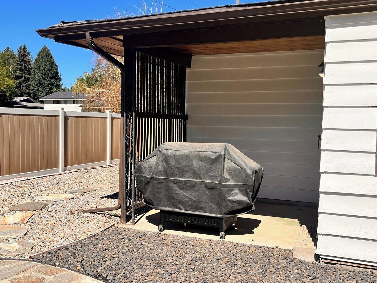 Un barbecue couvert se trouve à l’extérieur d’un bâtiment doté d’une terrasse en bois et d’un espace recouvert de gravier.