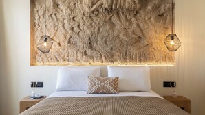 A bedroom with a textured stone wall, a bed with white linens, a patterned throw blanket, and two bedside tables with lamps.